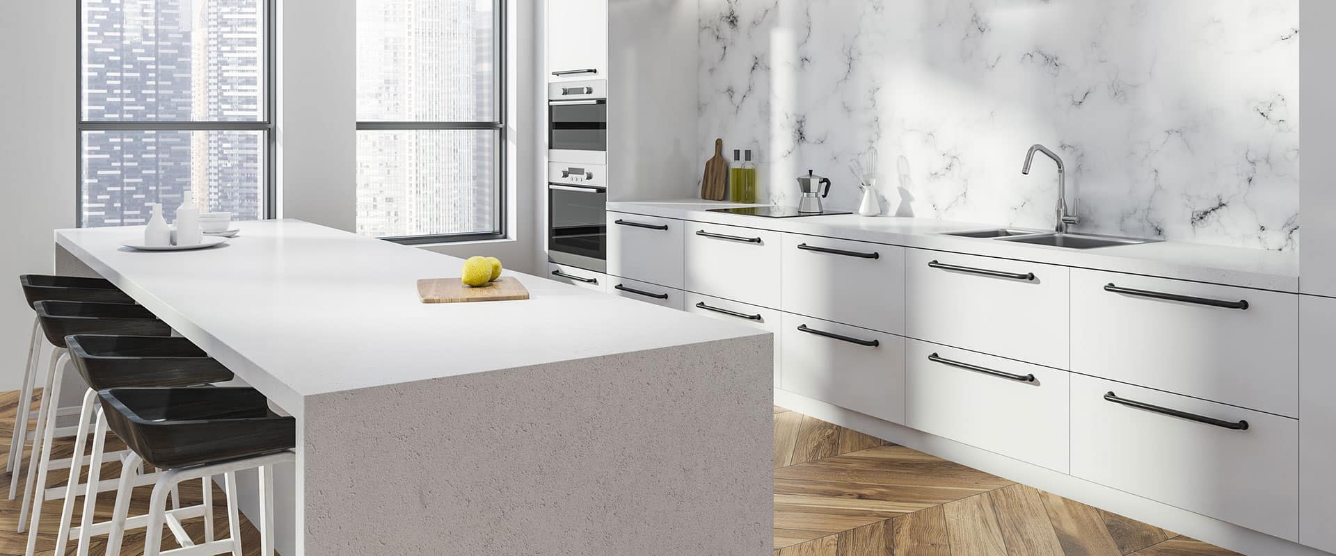 Modern kitchen with white cabinets and drawers, accented by sleek black handles and a pristine marble backsplash. Features a long island with black stools and a lemon on a cutting board. Large windows reveal a cityscape view, while herringbone wood flooring adds warmth—perfect for those considering marble restoration in Astoria NY.