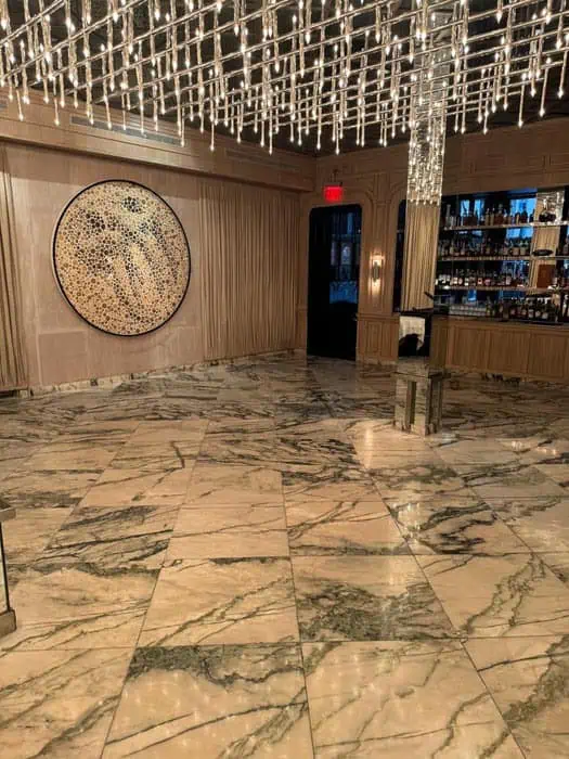 Luxurious interior with a marble floor, an intricate circular wall art, and a ceiling of hanging lights. A bar area with shelves filled with bottles is visible in the background, set against expertly restored stonework by premier restoration services in Manhattan, NY.