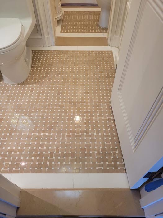 A bathroom featuring a beige and white basketweave mosaic tile floor showcases meticulous design. The white toilet and vanity add classic elegance, while the pattern extends into a smaller area. Perfect for anyone seeking marble restoration in Astoria, NY to maintain its charm.
