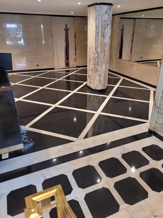 Luxurious interior with black and white marble tile flooring featuring a geometric pattern. A marble column stands in the center, surrounded by mirrored walls, reminiscent of expert stone restoration from Manhattan, NY. A partially visible desk and some cables are in the foreground.