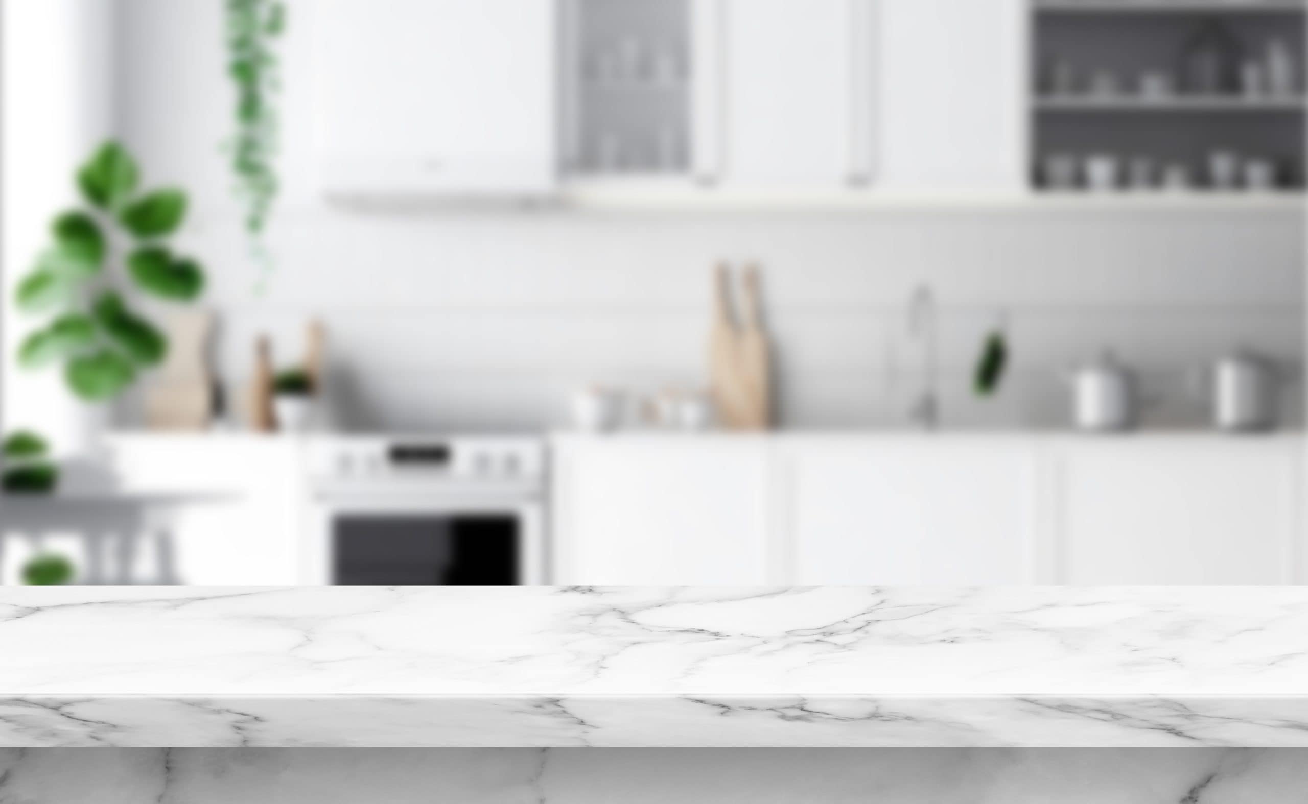 A stylish kitchen with a marble countertop in the foreground showcases expert marble restoration Astoria NY offers. The background features blurred white cabinetry, a stove, potted plants, and kitchen utensils, creating a modern and clean aesthetic.