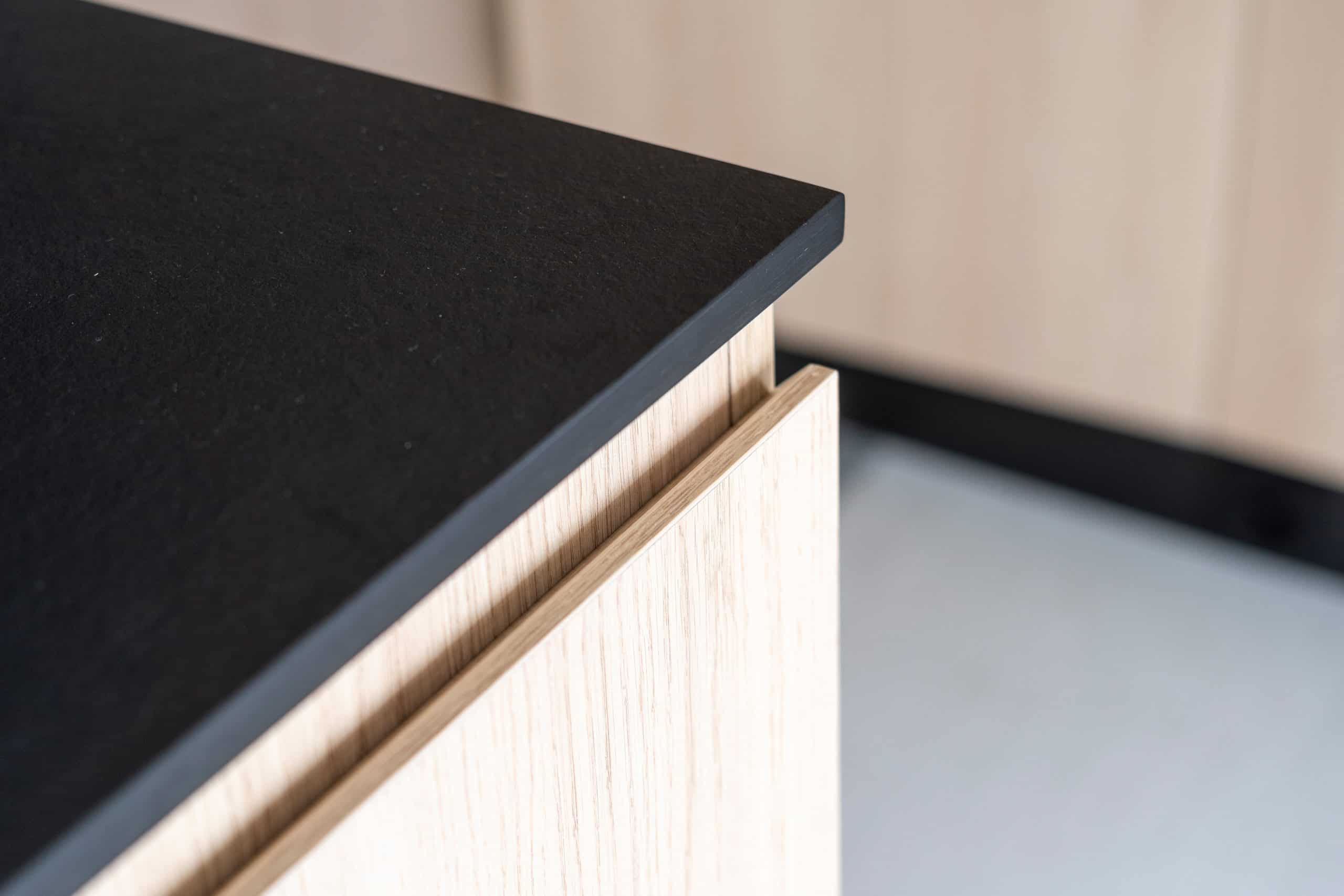 Close-up of a modern kitchen counter in Manhattan, NY, featuring a black countertop and light wood cabinetry. The image highlights the sleek design and sharp edges, showcasing stone restoration expertise that brings out the best in contemporary materials.