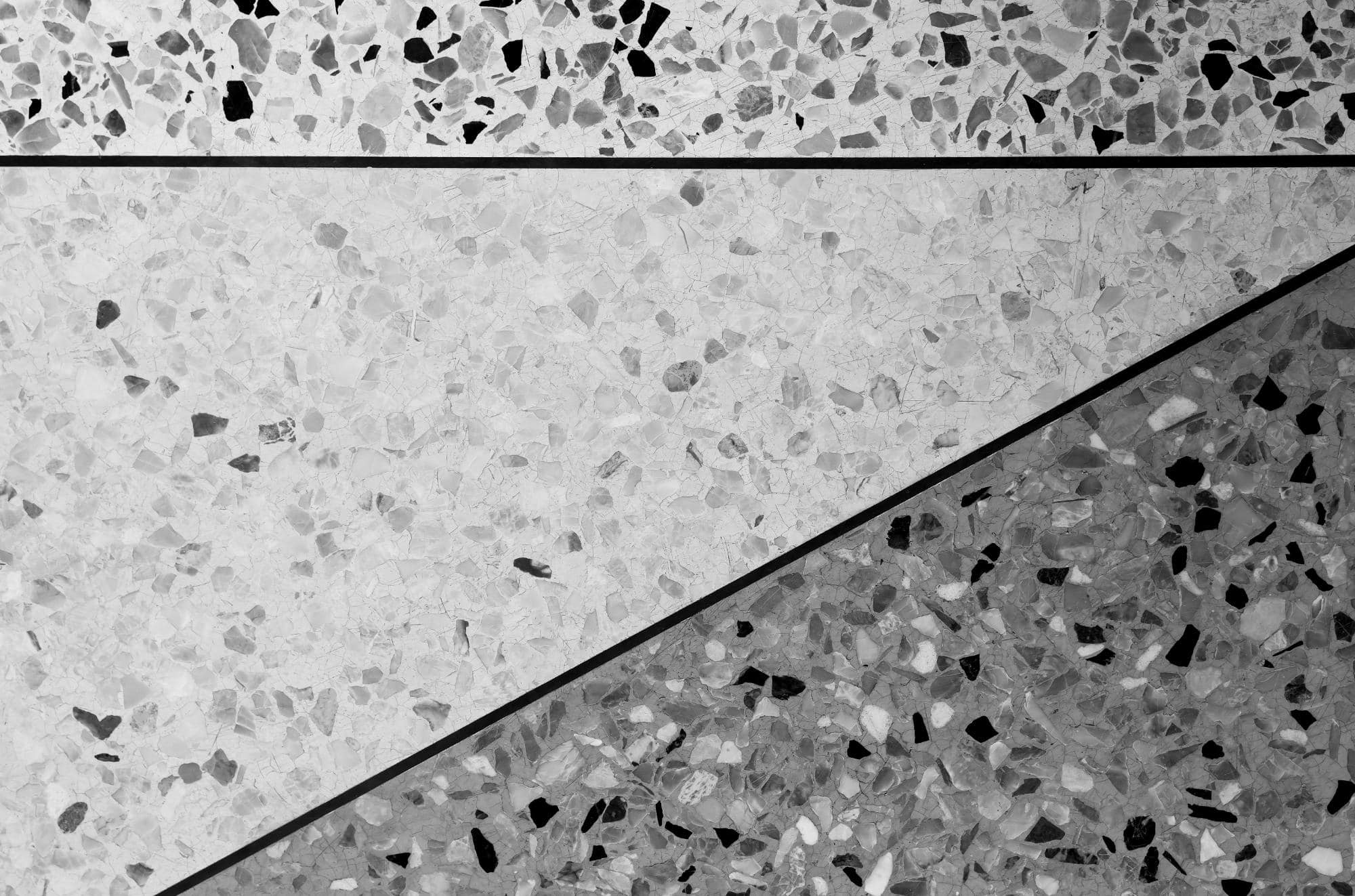 Black and white photo of a terrazzo floor divided into three triangular sections, each with a different shade and pattern of stone chips separated by thin dark lines.